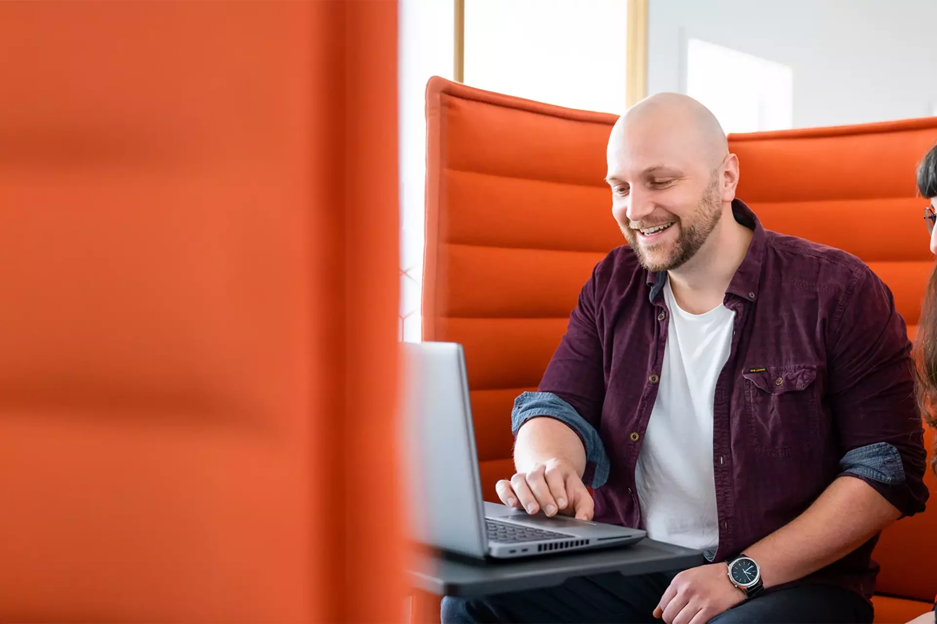 Zwei Mitglieder des Babtec-Teams arbeiten gemeinsam an einem Laptop auf einer orangefarbenen Couch.