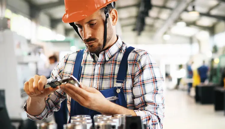 Ein Mitarbeiter prüft mit einem Messschieber die Qualität eines Produktes