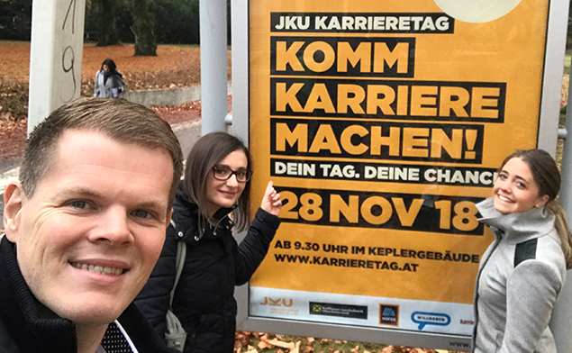 Drei Personen vor einem großen Plakat des JKU Karrieretags